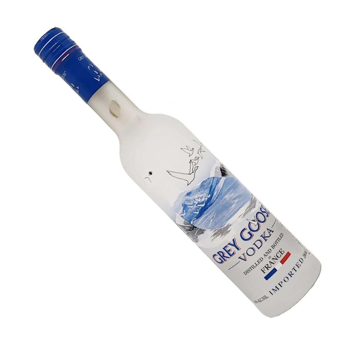 Garrafa Grey Goose Vodka inclinada, com tampa azul e rótulo branco ilustrado.