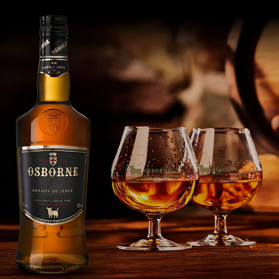 Garrafa de brandy de Jerez Osborne ao lado de duas tacas servidas, com barril de carvalho ao fundo.