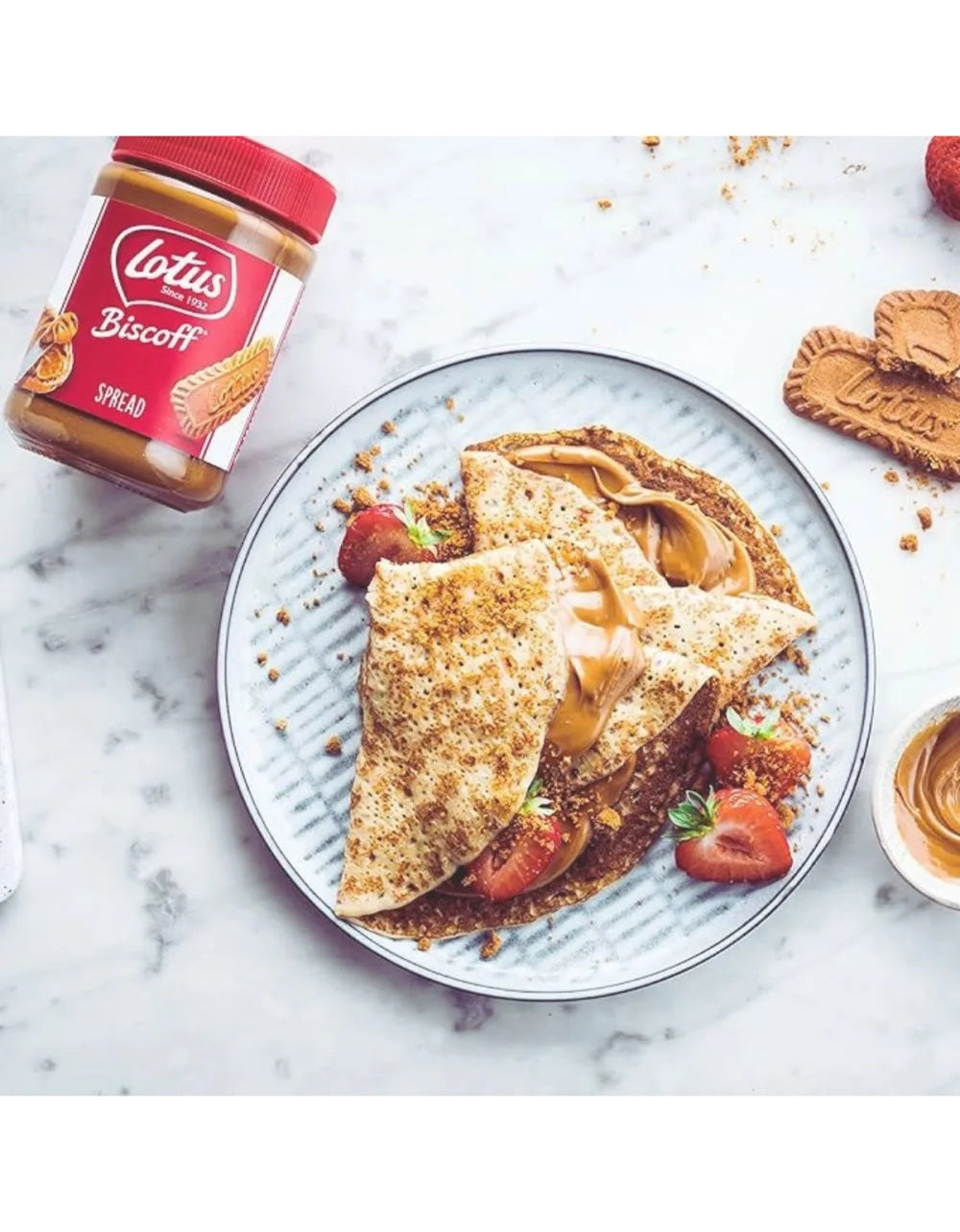 Pote Lotus Biscoff ao lado de crepes com morangos e pasta de biscoito.