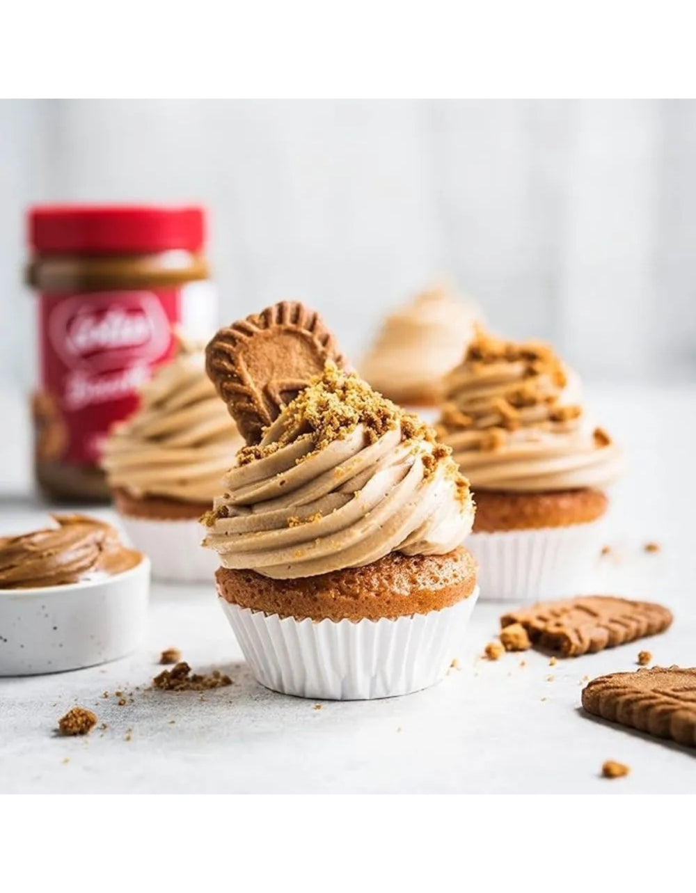Cupcake decorado com creme, farelos e biscoito Biscoff, com o pote ao fundo.