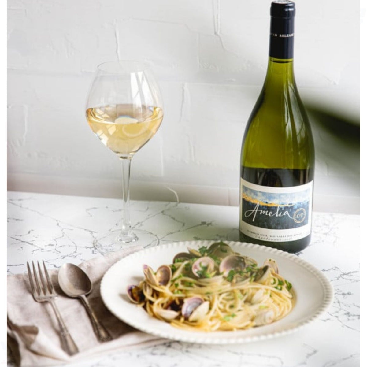 Garrafa de vinho Amelia ao lado de uma taça e um prato de massa com frutos do mar.