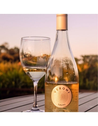 Garrafa de vinho Veroni Go Sauvi ao lado de uma taça com vinho branco em ambiente externo.