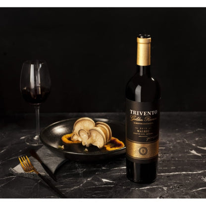 Garrafa de Trivento Golden Reserve Malbec ao lado de uma taça e prato com cogumelos.