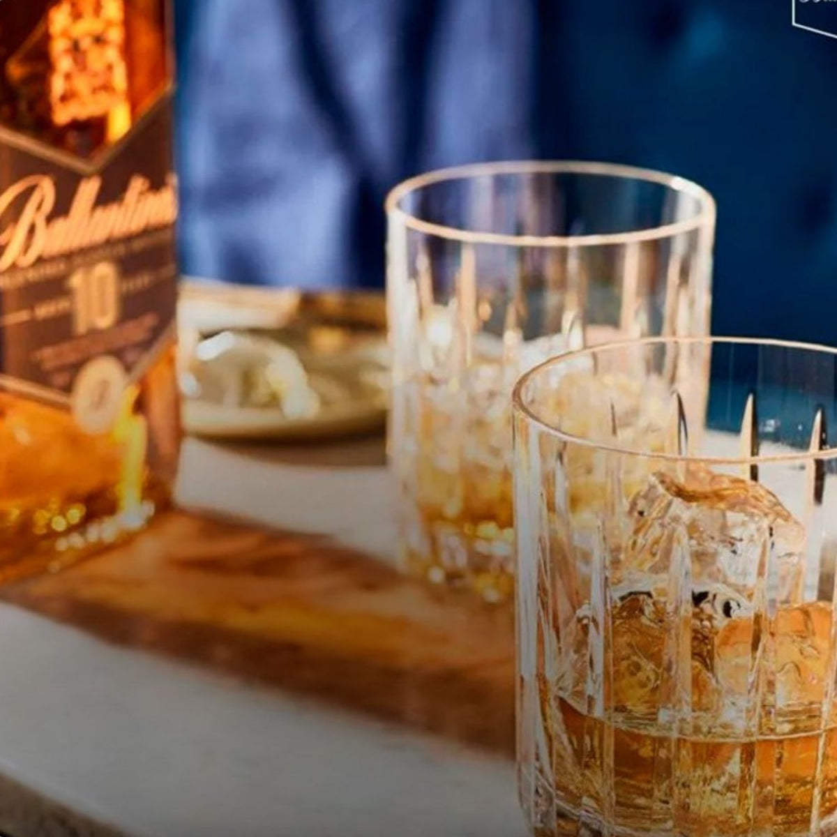 Whisky Ballantine's servido com gelo em copos, com a garrafa ao fundo.